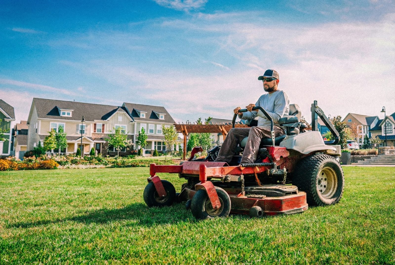 A lawn care professional mowing a lush green suburban lawn on a riding mower